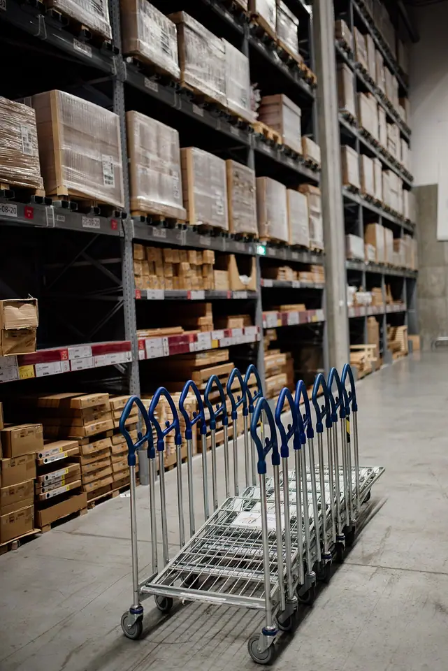 A warehouse aisle with boxes, stock and handling carts.